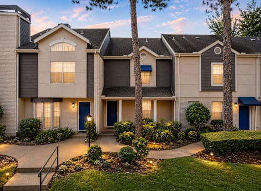 A well-lit residential building with a front yard and a tree.