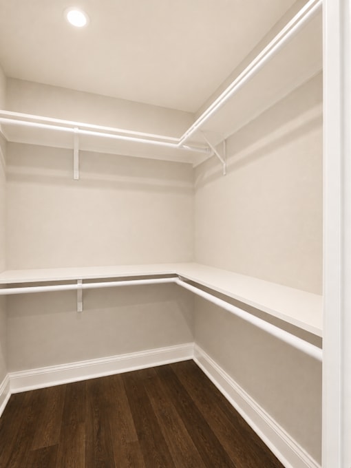 Empty walk-in closet with white shelves and wooden floors.