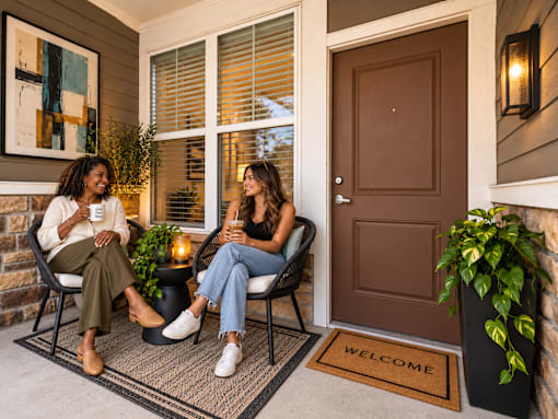 Two women sitting on chairs on a porch with a welcome mat.
