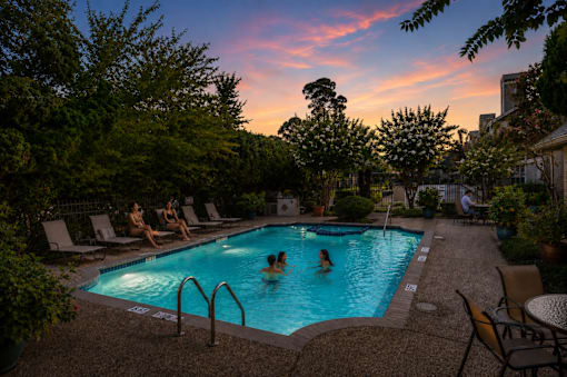 A swimming pool surrounded by trees and people enjoying the water.