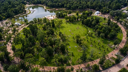 A park with a large pond and a grassy area with people walking around.