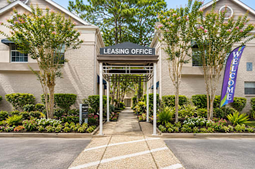 A leasing office is surrounded by a landscaped area with a welcome sign.