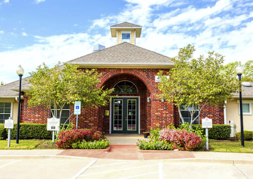 the front of Addison Park Apartments in Arlington, TX with trees and flowers