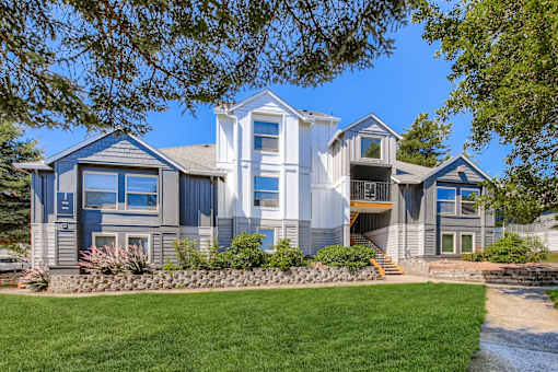 A large house with a grey and blue exterior and a stone wall in front.