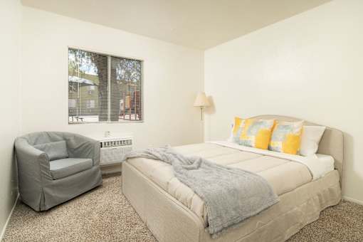 A bedroom with a bed, chair, and window.