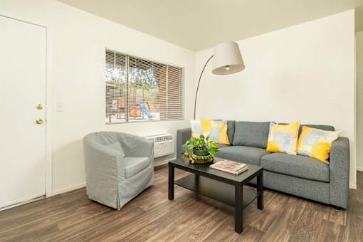 A grey couch with yellow pillows sits in a living room with a grey armchair and a coffee table.