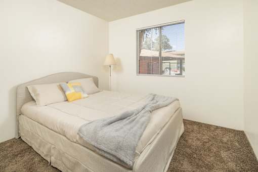 A bedroom with a bed, pillows, a blanket, a lamp, and a picture of a house on the wall.