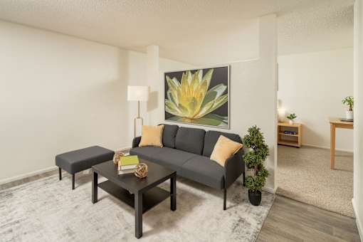 A grey sofa with a yellow pillow is in the middle of a room with a large painting of a yellow flower on the wall.