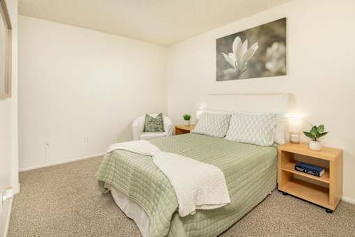 A bedroom with a bed, nightstand, and a picture on the wall.