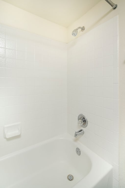 A white bathroom with a white tub and a shower head.