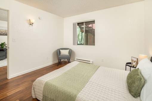 A bedroom with a bed, chair, and window.