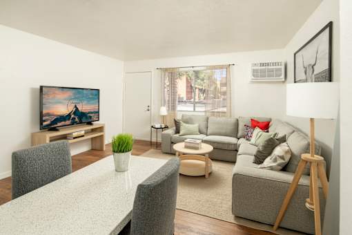 A living room with a grey couch, a white dining table and a painting on the wall.