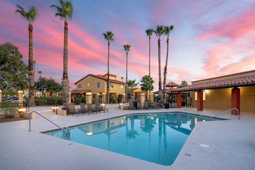 A swimming pool surrounded by palm trees and a building in the background.