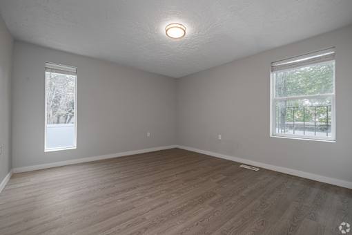 Empty room with wooden flooring and two windows.
