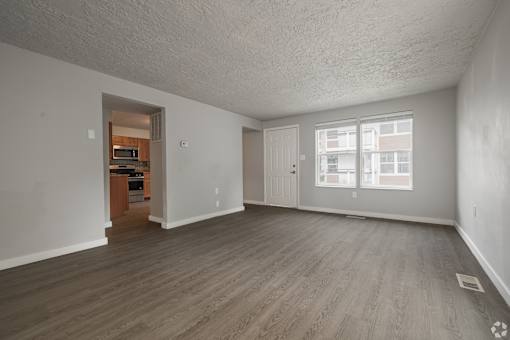 A spacious empty room with wooden flooring and a doorway leading to another room.