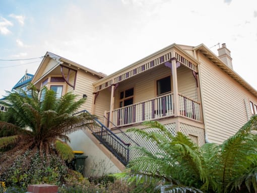 a yellow house with a white railing and a palm tree in front of it