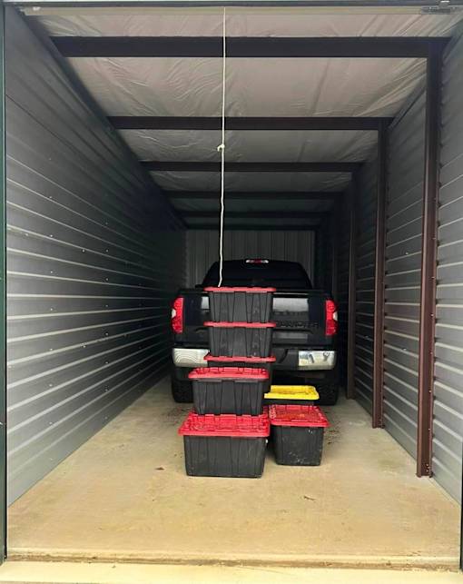 A black car is parked in a garage with several black and red containers on the floor.