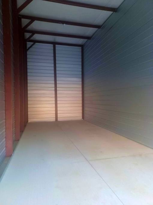 A long, narrow storage space with a white floor and closed, white doors.
