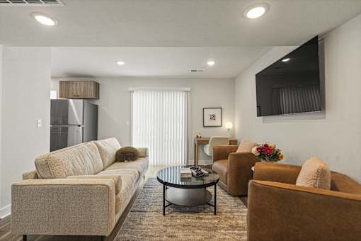 A living room with a beige couch, a coffee table, and a flat screen TV mounted on the wall.