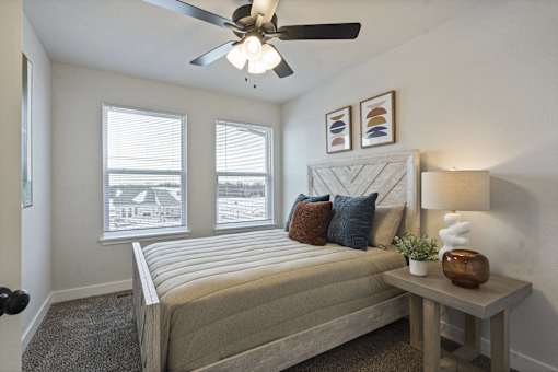 A bedroom with a bed, a ceiling fan, and a small table with a plant and a vase on it.