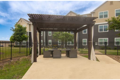 a patio with a table and chairs under a pergola in front of an apartment building