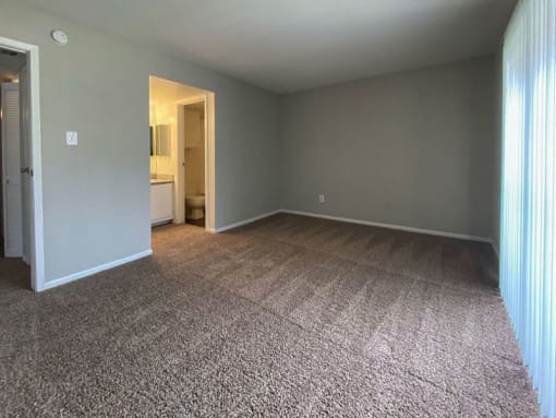 an empty bedroom with a bathroom in the background