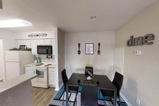 a dining area with a table and chairs and a kitchen in the background