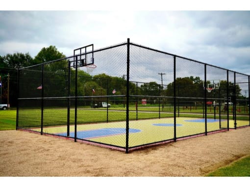 a basketball court with a hoop on a dirt ground and trees in the background