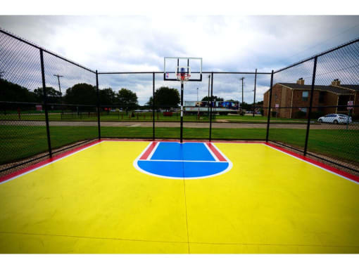 a yellow and blue basketball court with a red brick building in the background
