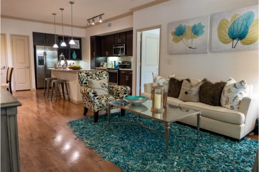 a living room with a couch coffee table and chairs and a kitchen in the background
