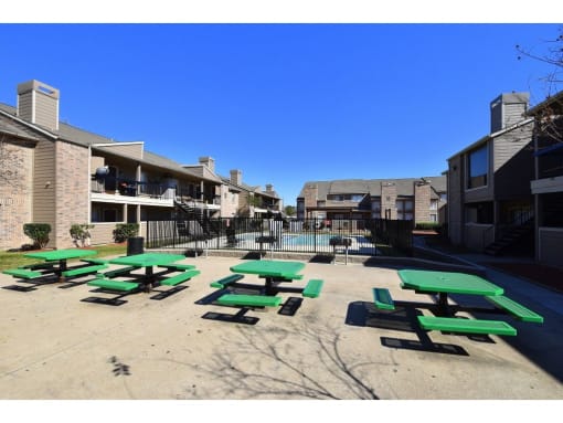 a courtyard with green picnic tables and a pool in the background