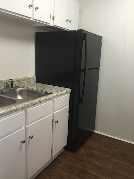 A black refrigerator stands next to a sink in a kitchen.