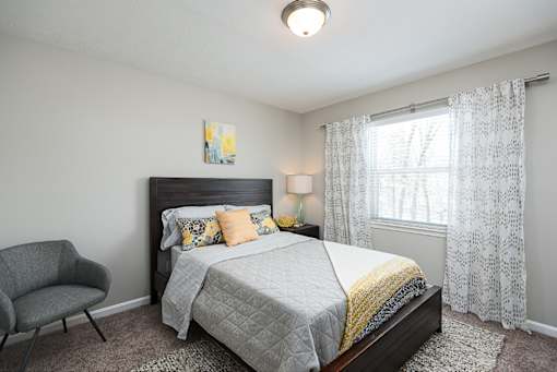 A bedroom with a bed, chair, and window.