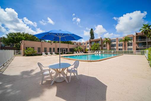 A pool area with a table and chairs and a blue umbrella.