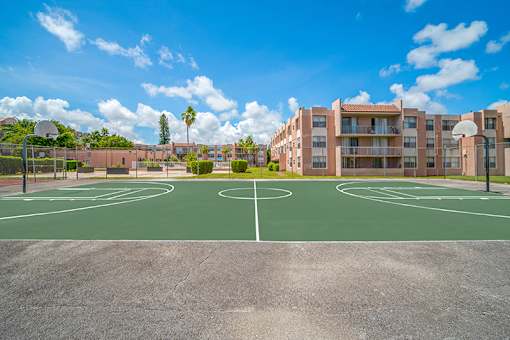 A basketball court in front of apartment buildings on a sunny day.