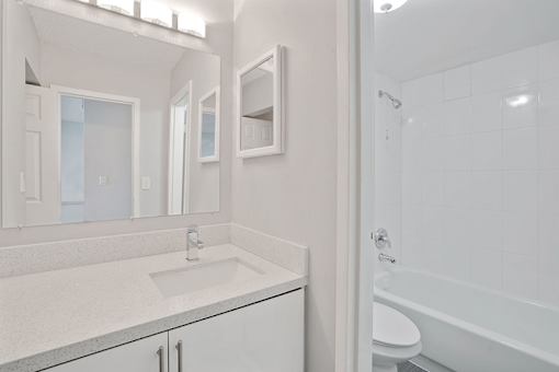 A white bathroom with a sink, mirror, and bathtub.