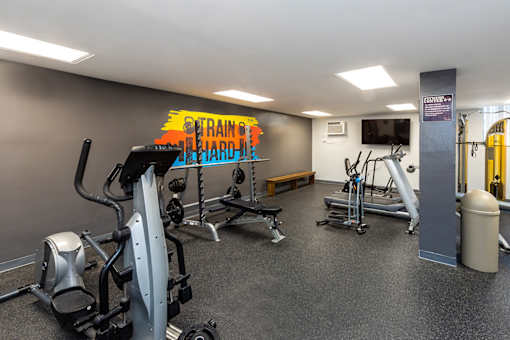 A gym with a variety of equipment including a treadmill, a bench, and a television.