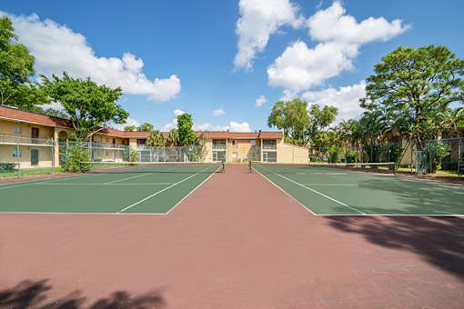 A tennis court is surrounded by apartment buildings.