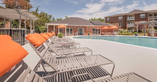 A pool with orange sun loungers and a building in the background.