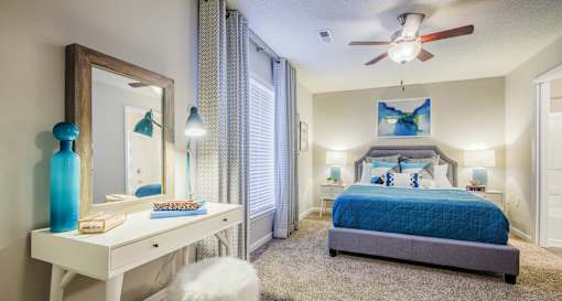 A bedroom with a blue bedspread and a white dresser with a mirror.