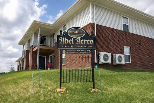 A sign for Abel Acre Apartments stands in front of a brick building.