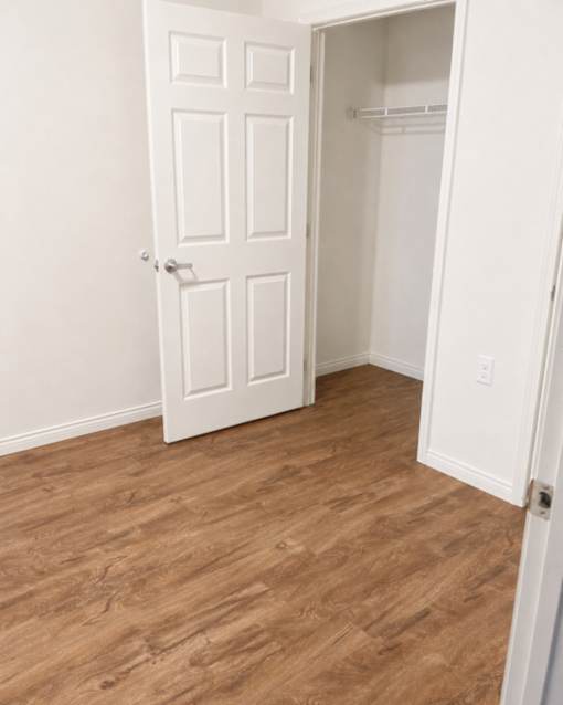 A white door is open to a room with wood flooring.