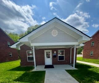 A small brick house with a white roof and a covered front porch.