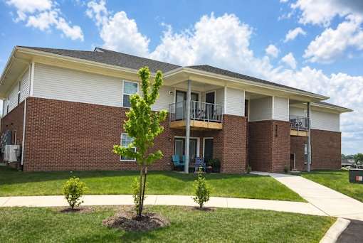A small tree is in front of a two-story apartment building.