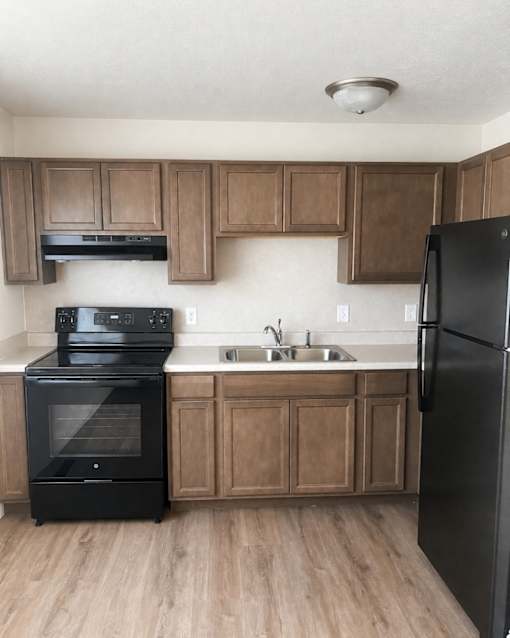 A black refrigerator is in a kitchen with wooden cabinets.