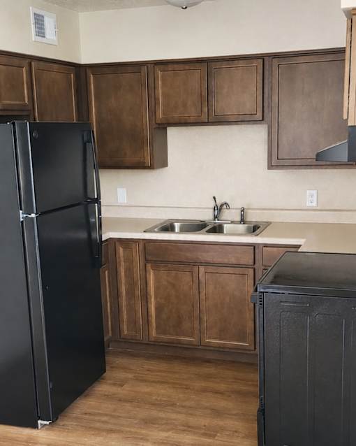A black refrigerator stands in a kitchen with wooden cabinets.