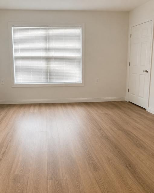 A room with a wooden floor and a window with blinds.