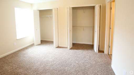 A room with three open closets and a carpeted floor.