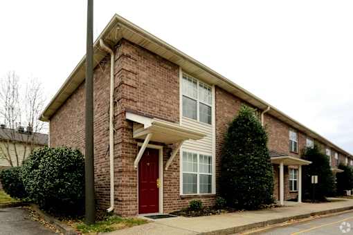 A red door is on the left side of a brick house.