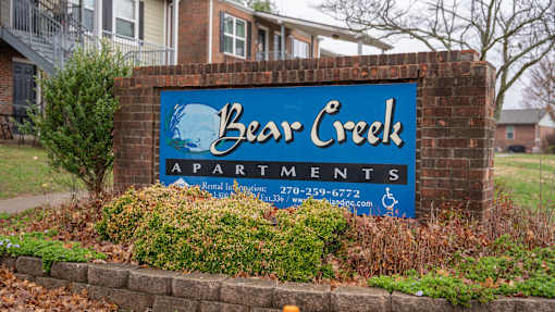 A sign for Bear Creek Apartments is displayed in front of a brick wall.